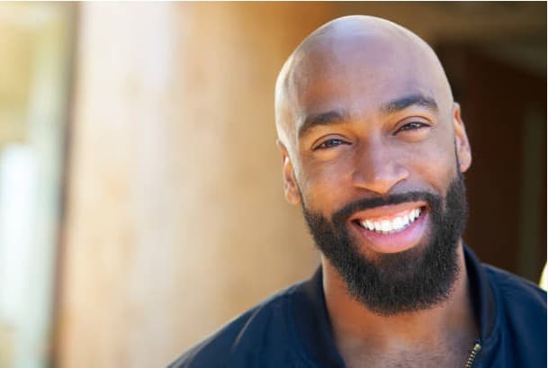 A smiling bald Black man with a neatly groomed beard and bright white teeth.