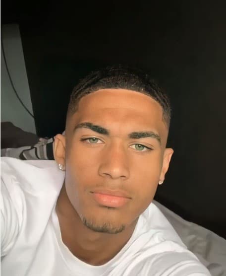 A young man with light green eyes, short dark hair, and small diamond earrings.