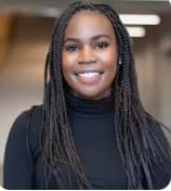 A smiling Black woman with long dark braids wearing a black turtleneck sweater.