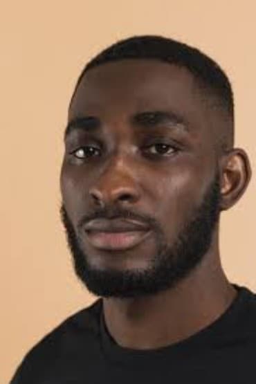 Young Black man with a short beard and buzz cut against a neutral beige backdrop.