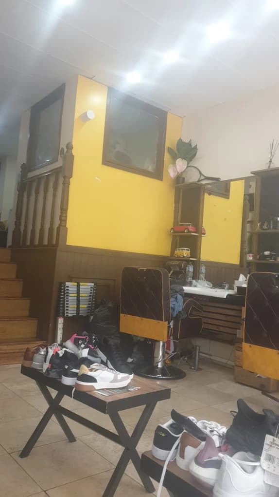 A bright barbershop interior with yellow walls, barber chairs, and sneakers displayed on wooden tables.